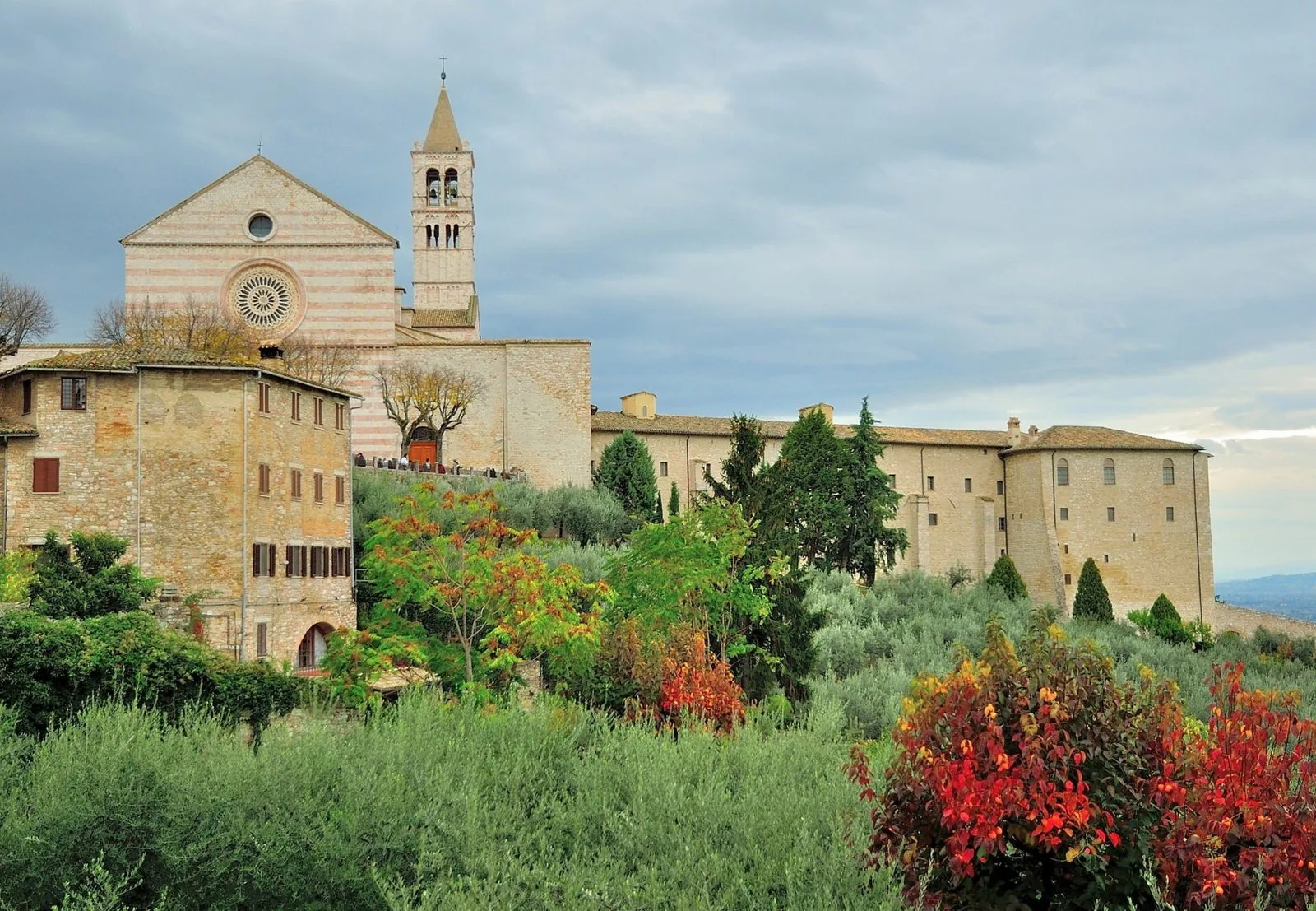 Basilica di Santa Chiara ad Assisi con alberi e cespugli dai colori autunnali in primo piano
